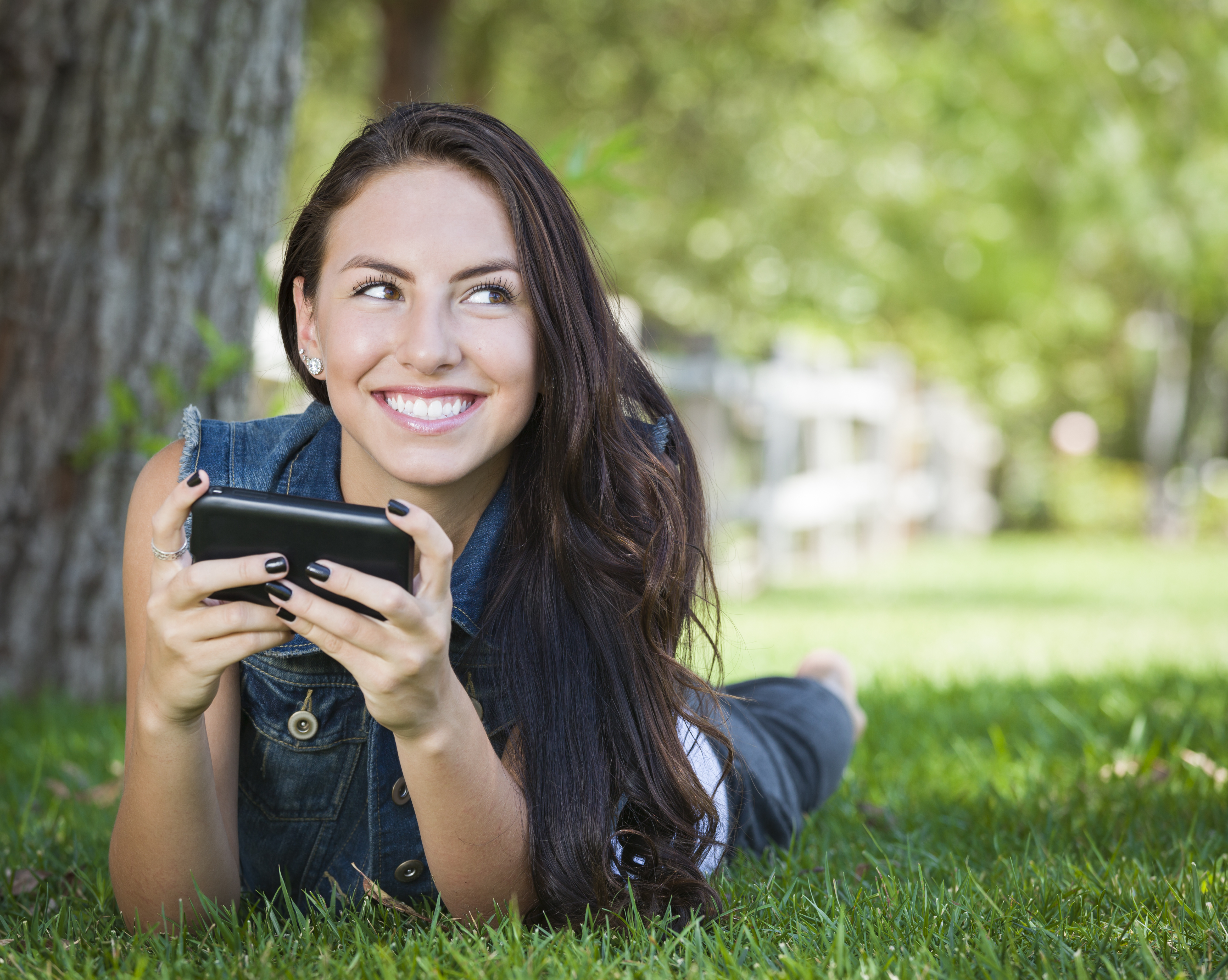 Attractive Happy Mixed Race Young Female Texting on Her Cell Phone Outside Laying in the Grass.