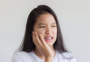 Teen girl using her hands to soothe a hurting mouth because of braces.